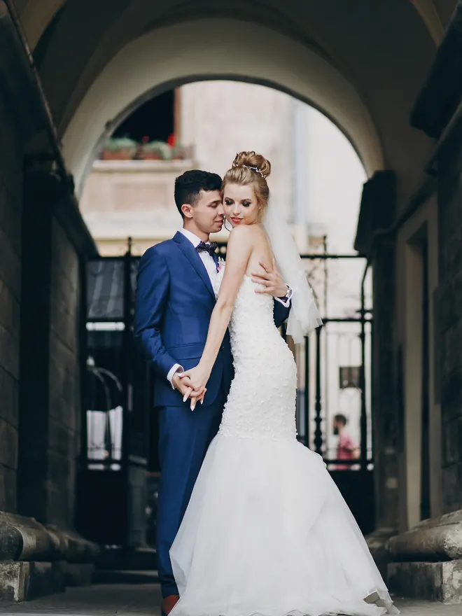 A bride and groom embracing beneath a stone archway