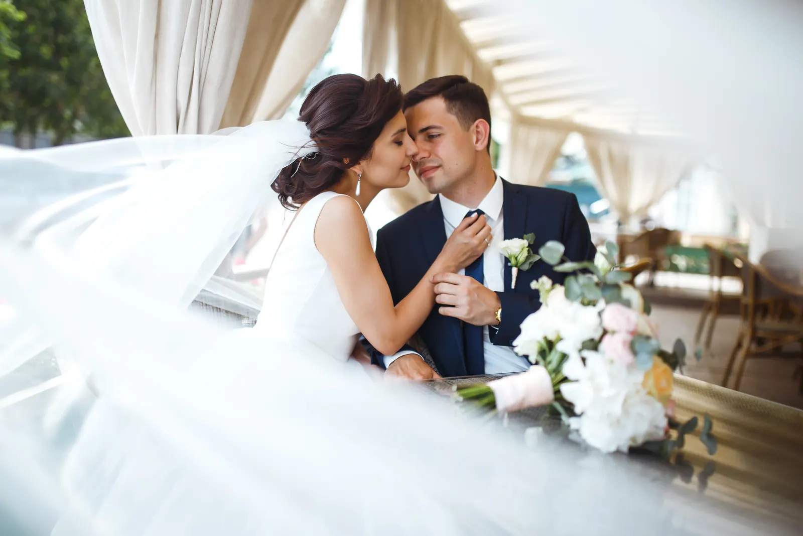 A bride leans in close to her groom while her veil drifts across the frame